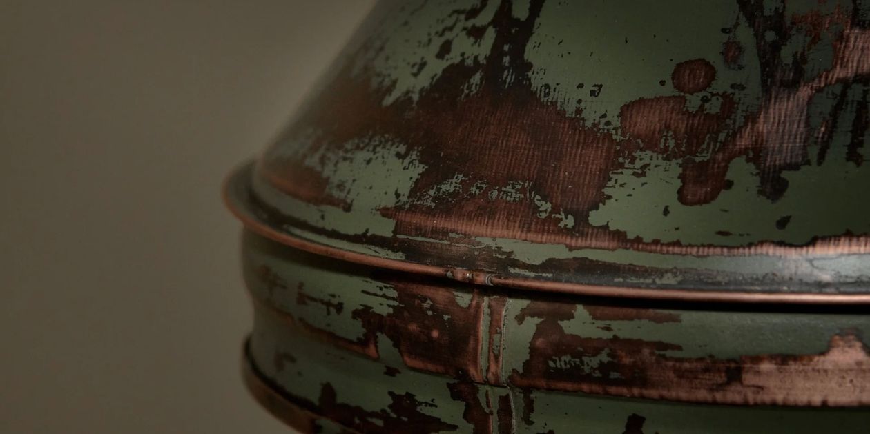 Close detail of a pendant lamp shade, its pale green paint worn back to bare copper.